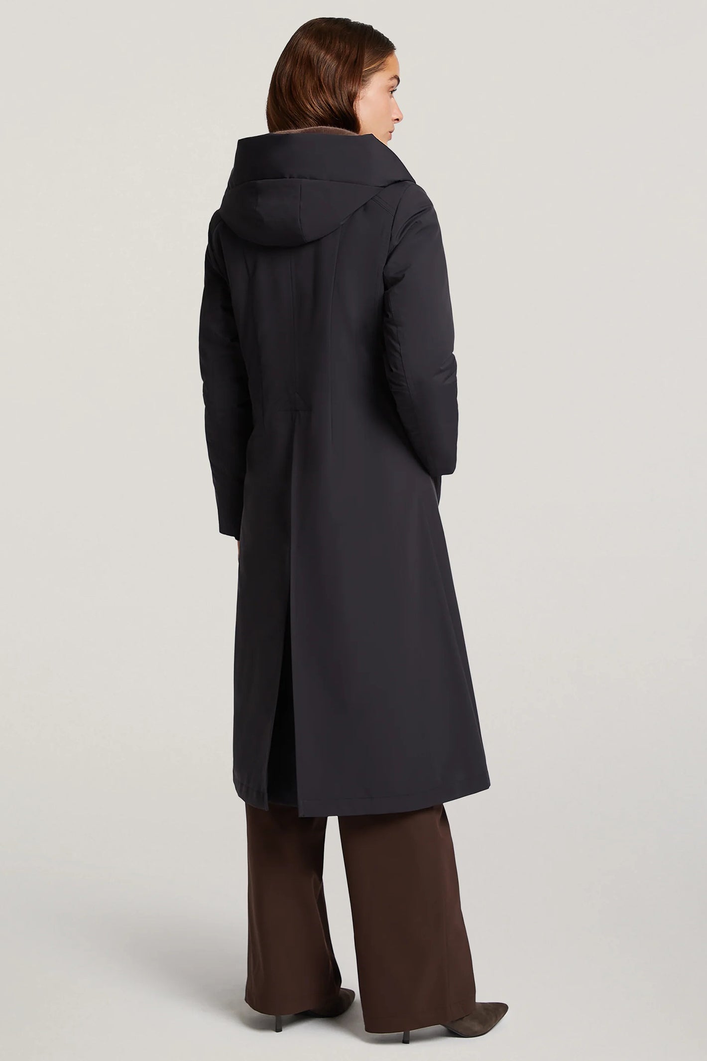 Person wearing a long dark coat on a light gray background