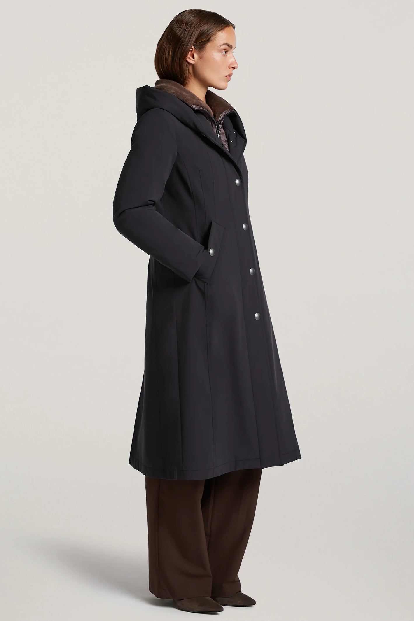 Woman wearing a black coat with fur lining on a light gray background