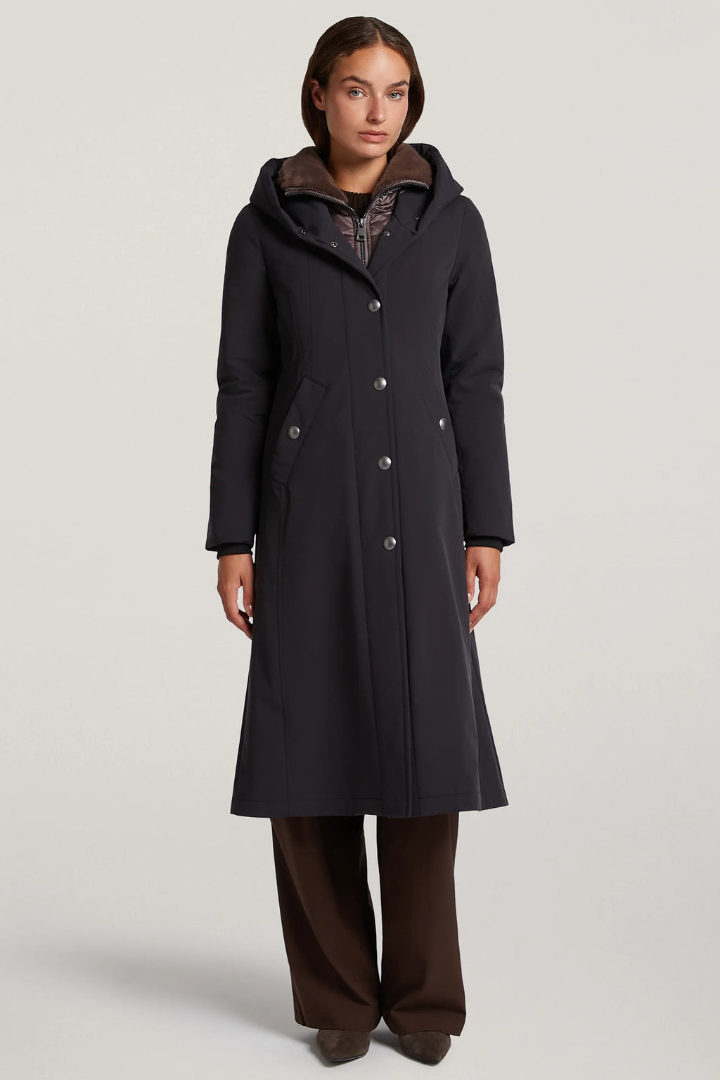 Woman wearing a long black coat with a hood on a light gray background