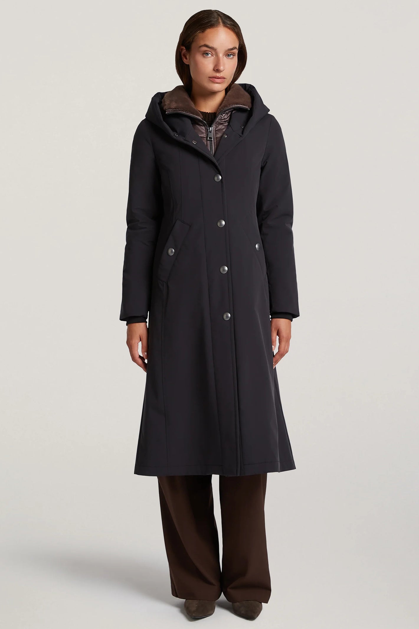 Woman wearing a long black coat with a hood on a light gray background