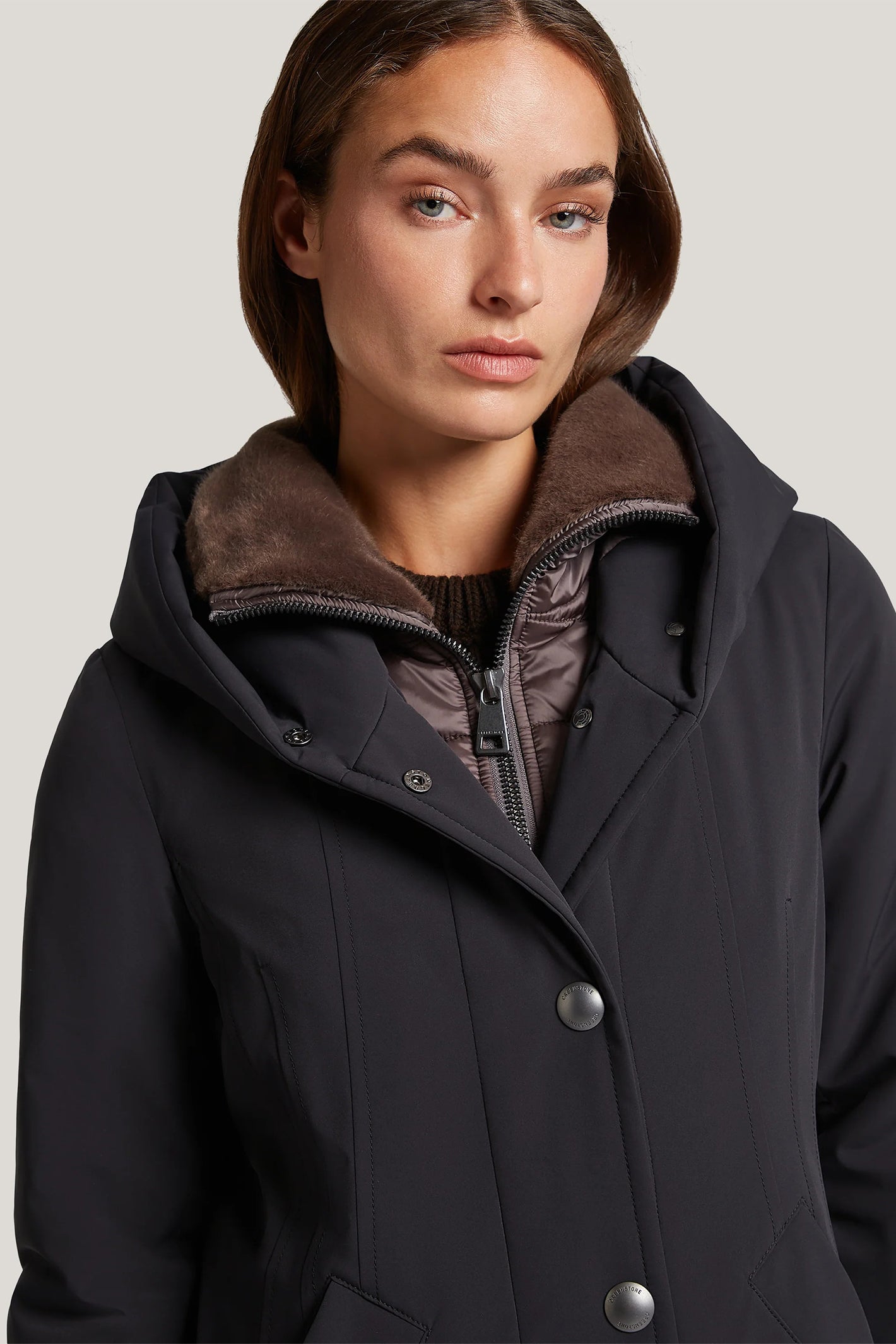 Woman wearing a black coat with a brown collar against a plain background