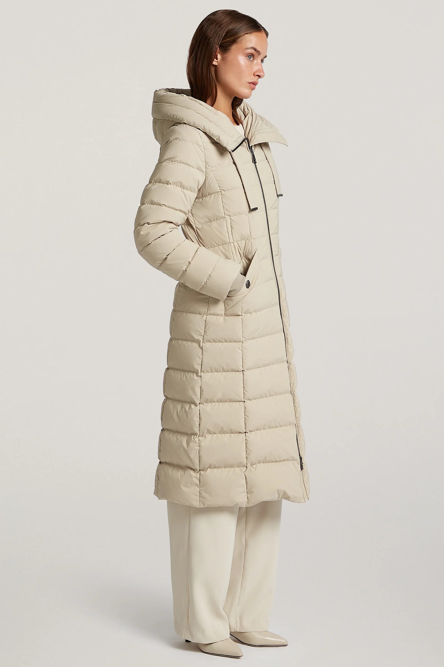 Woman wearing a beige puffer coat on a light gray background