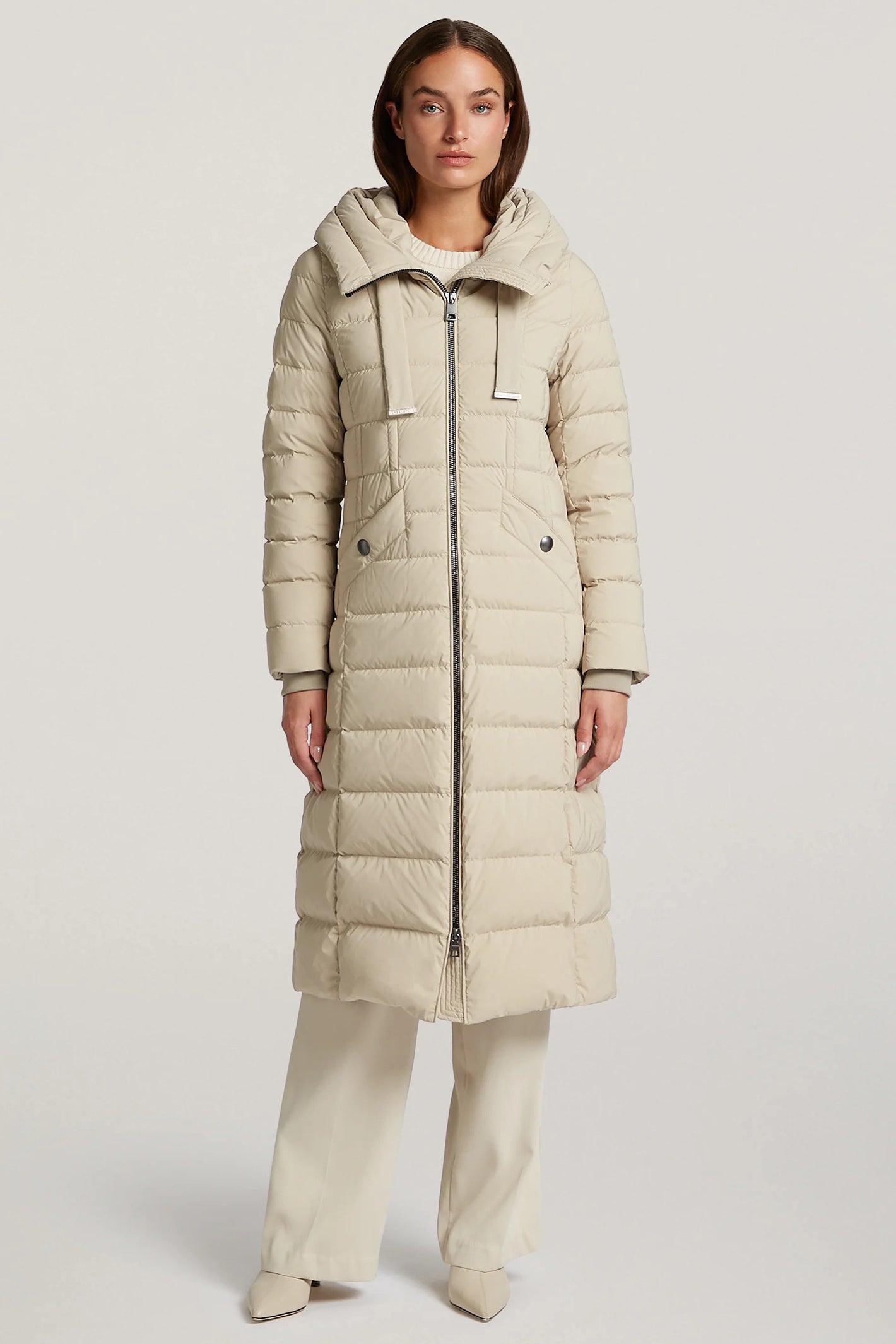 Woman wearing a beige long puffer coat on a white background