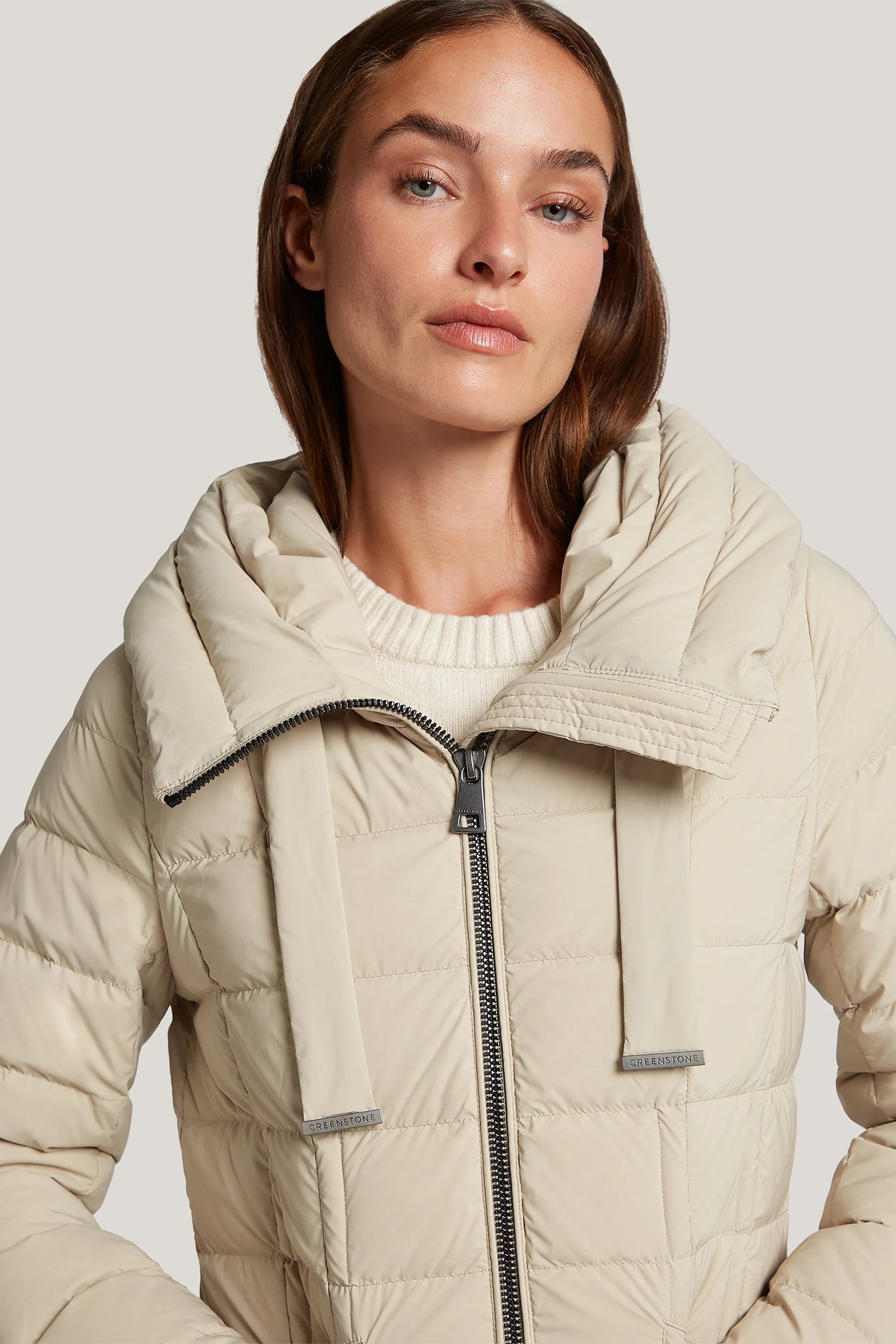 Woman wearing a beige puffer jacket on a plain background