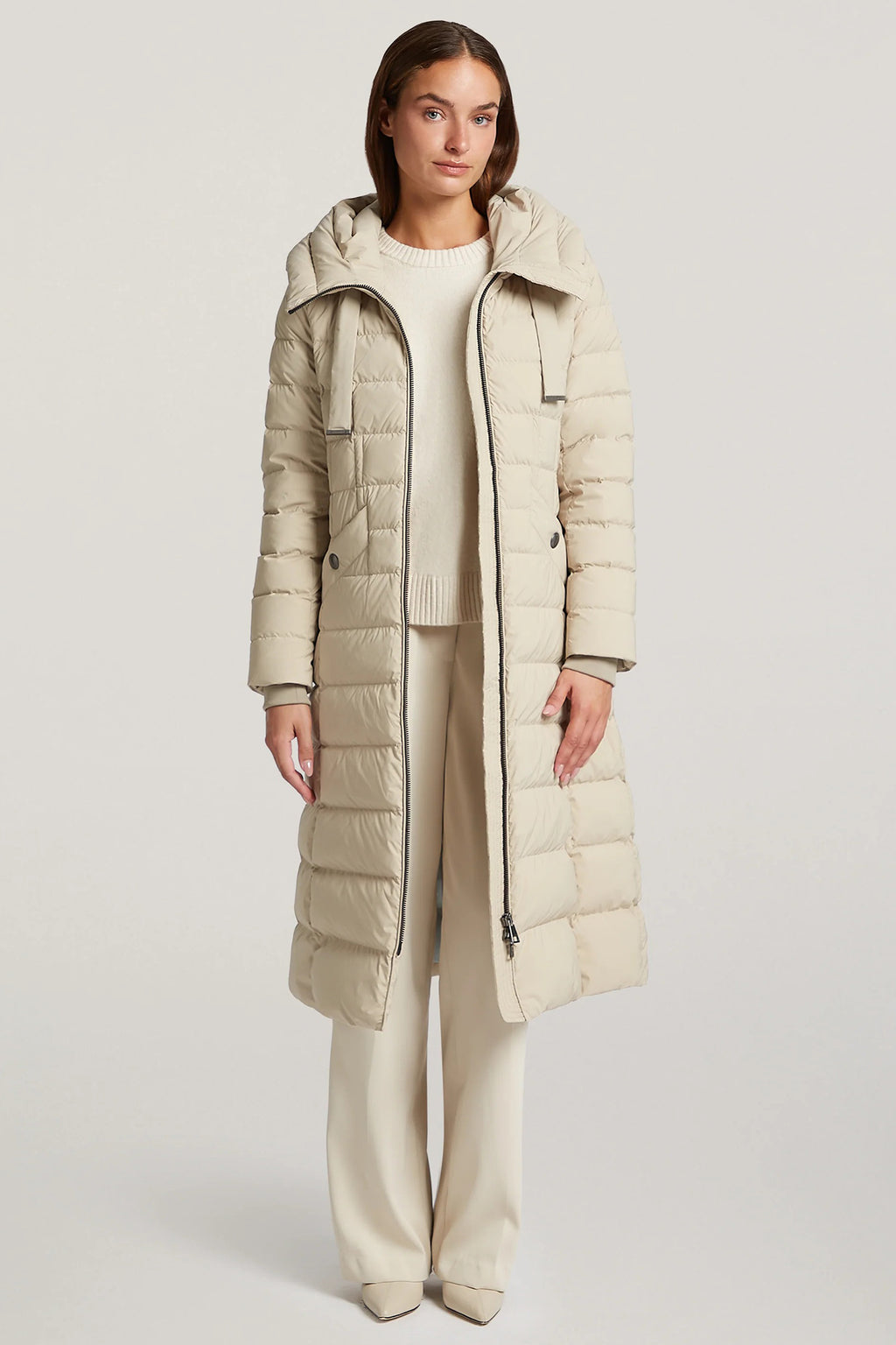 Woman wearing a long beige puffer coat on a white background