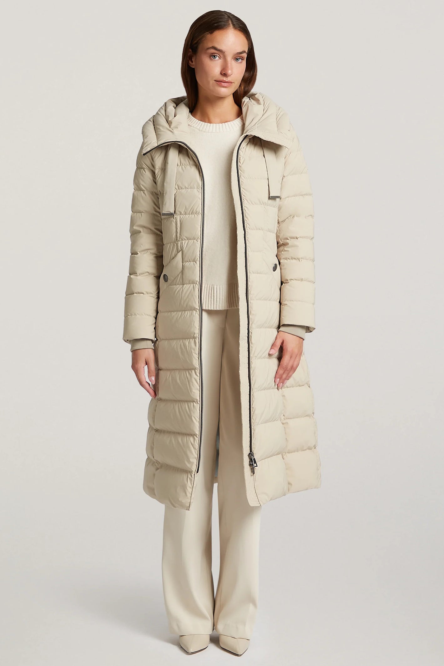 Woman wearing a long beige puffer coat on a white background