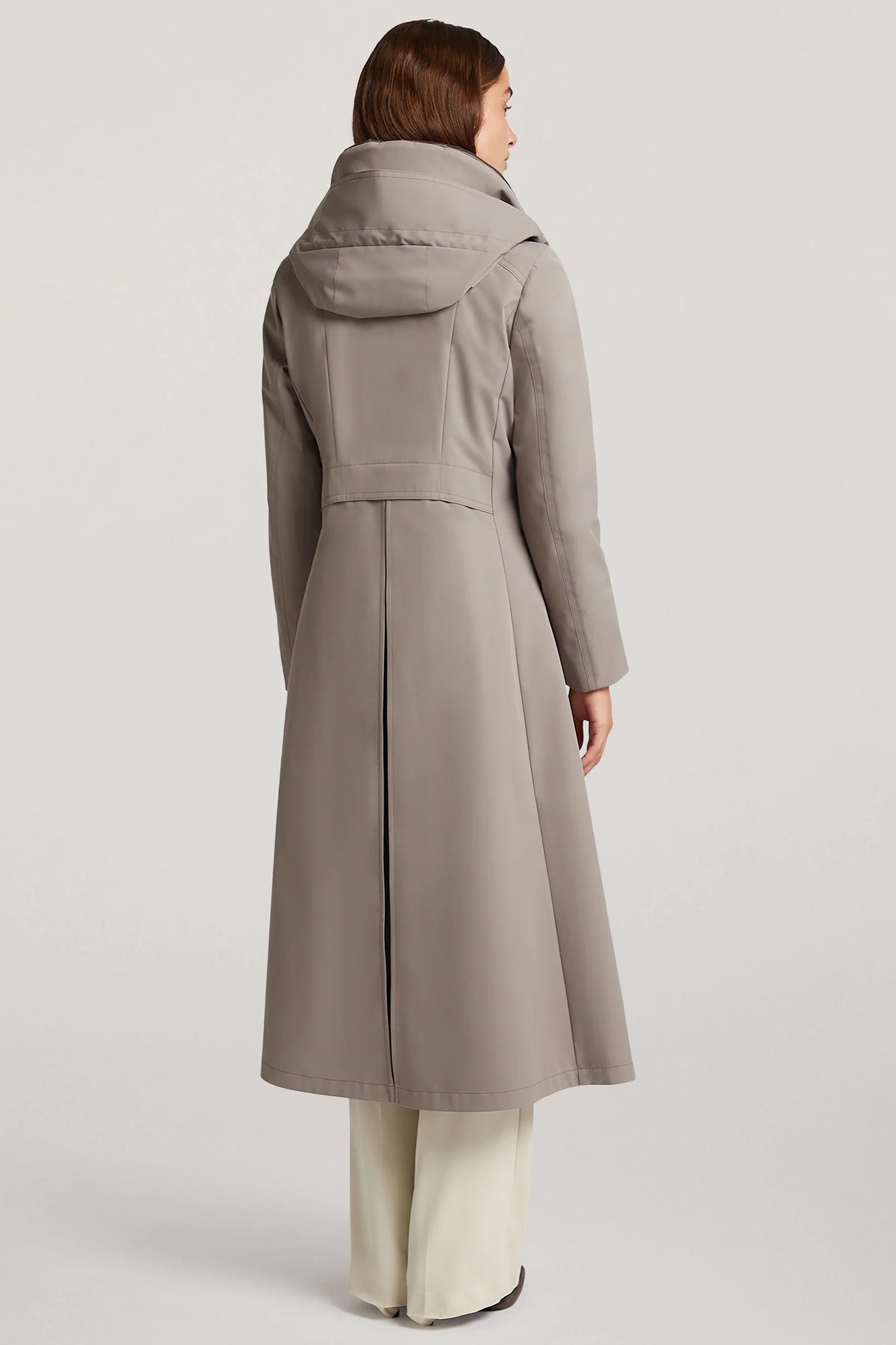 Woman wearing a long gray coat on a plain background