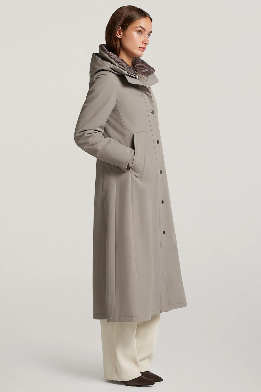 Woman wearing a long gray coat with a hood on a light gray background