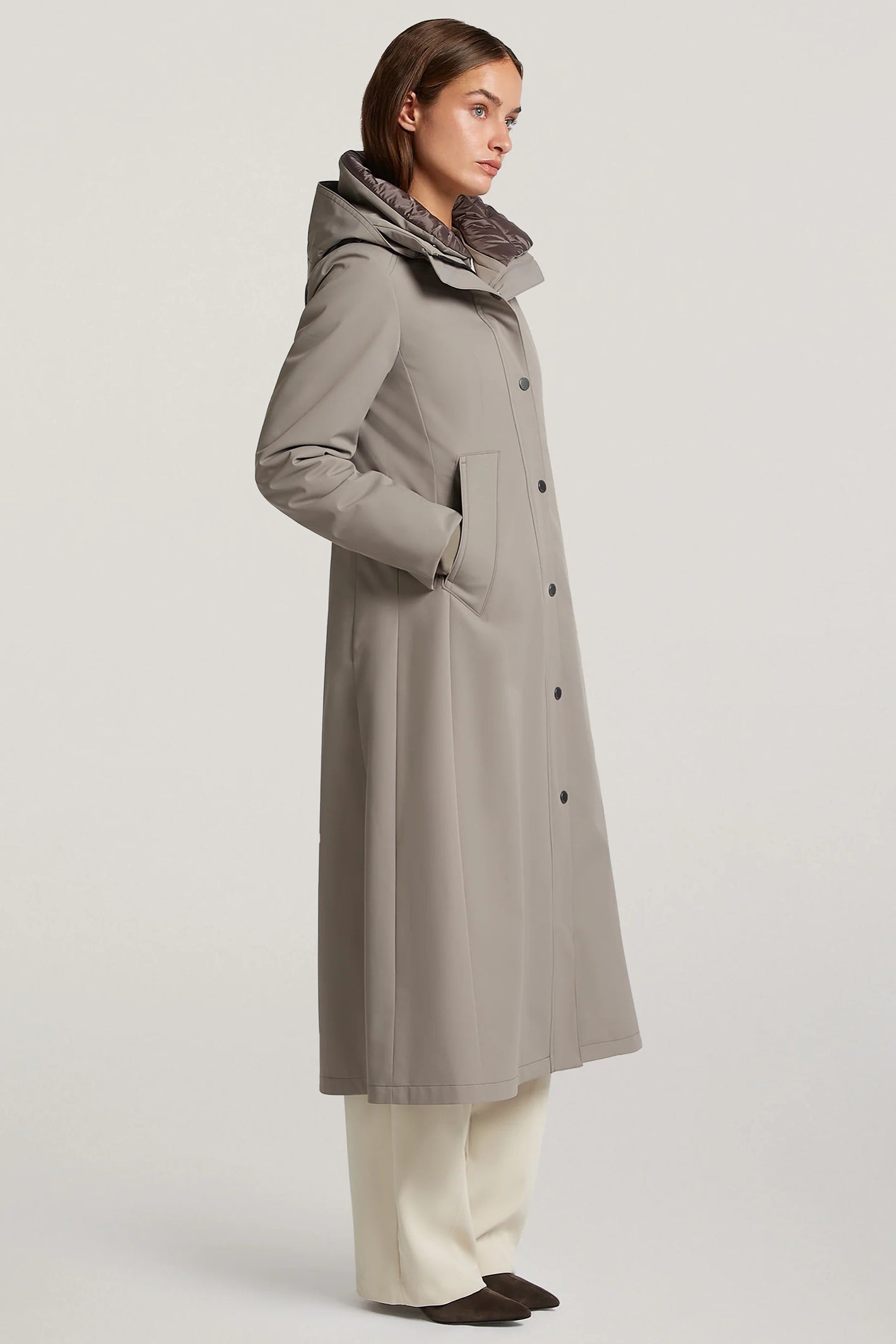 Woman wearing a long gray coat with a hood on a light gray background