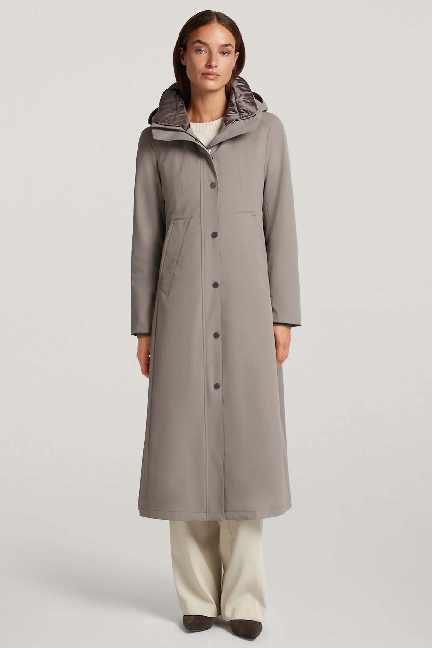 Woman wearing a long gray coat with a hood on a light background