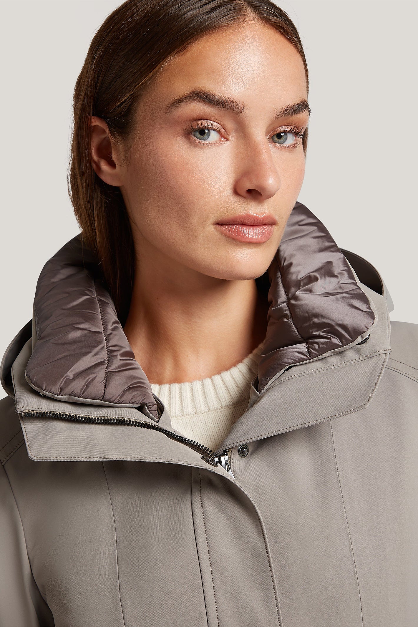 Woman wearing a gray coat with a hood on a plain background