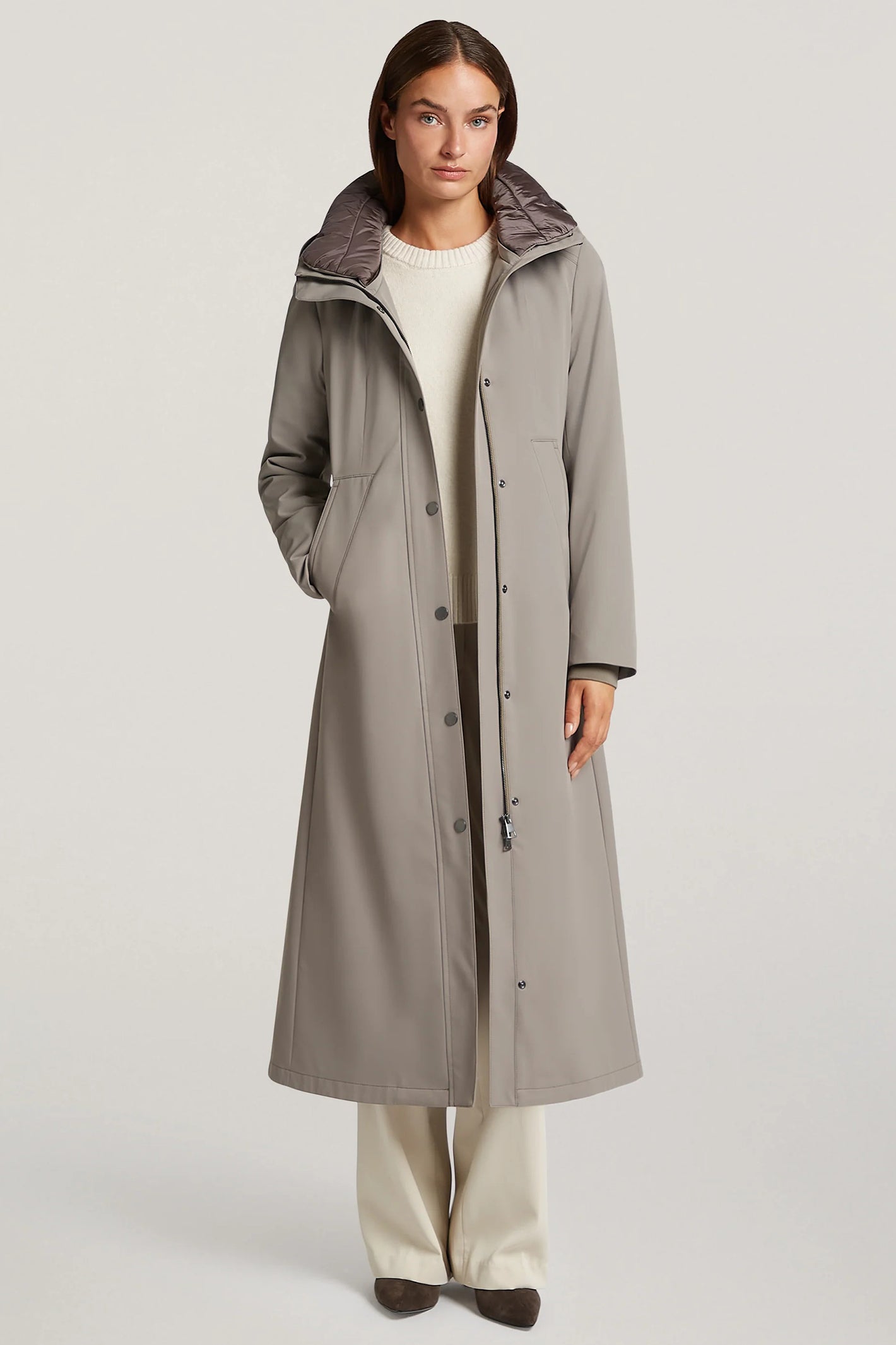 Woman wearing a long gray coat with a hood on a light gray background
