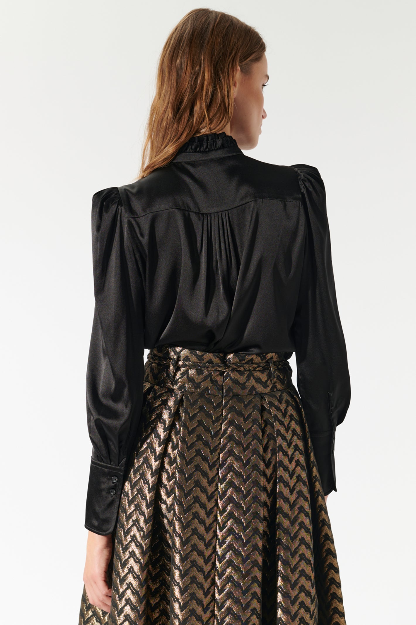 Woman wearing a black blouse with puffed sleeves and a patterned skirt on a white background
