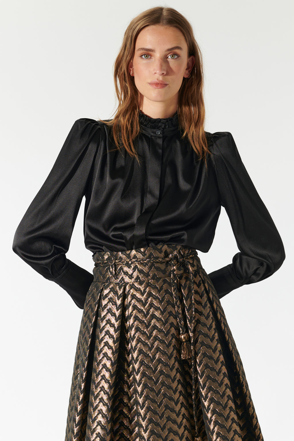Woman wearing a black blouse with long sleeves and a patterned skirt on a white background