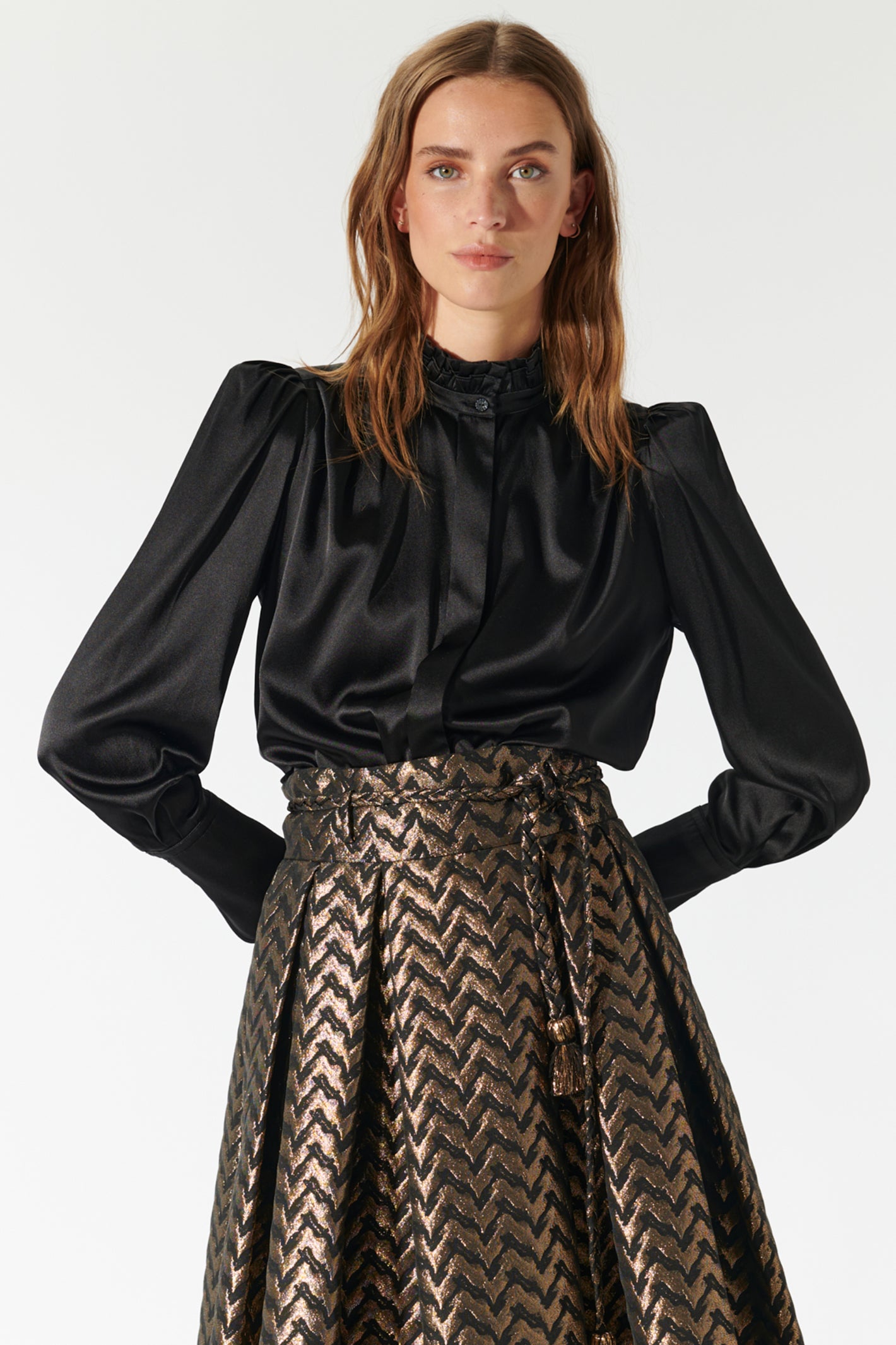 Woman wearing a black blouse with long sleeves and a patterned skirt on a white background