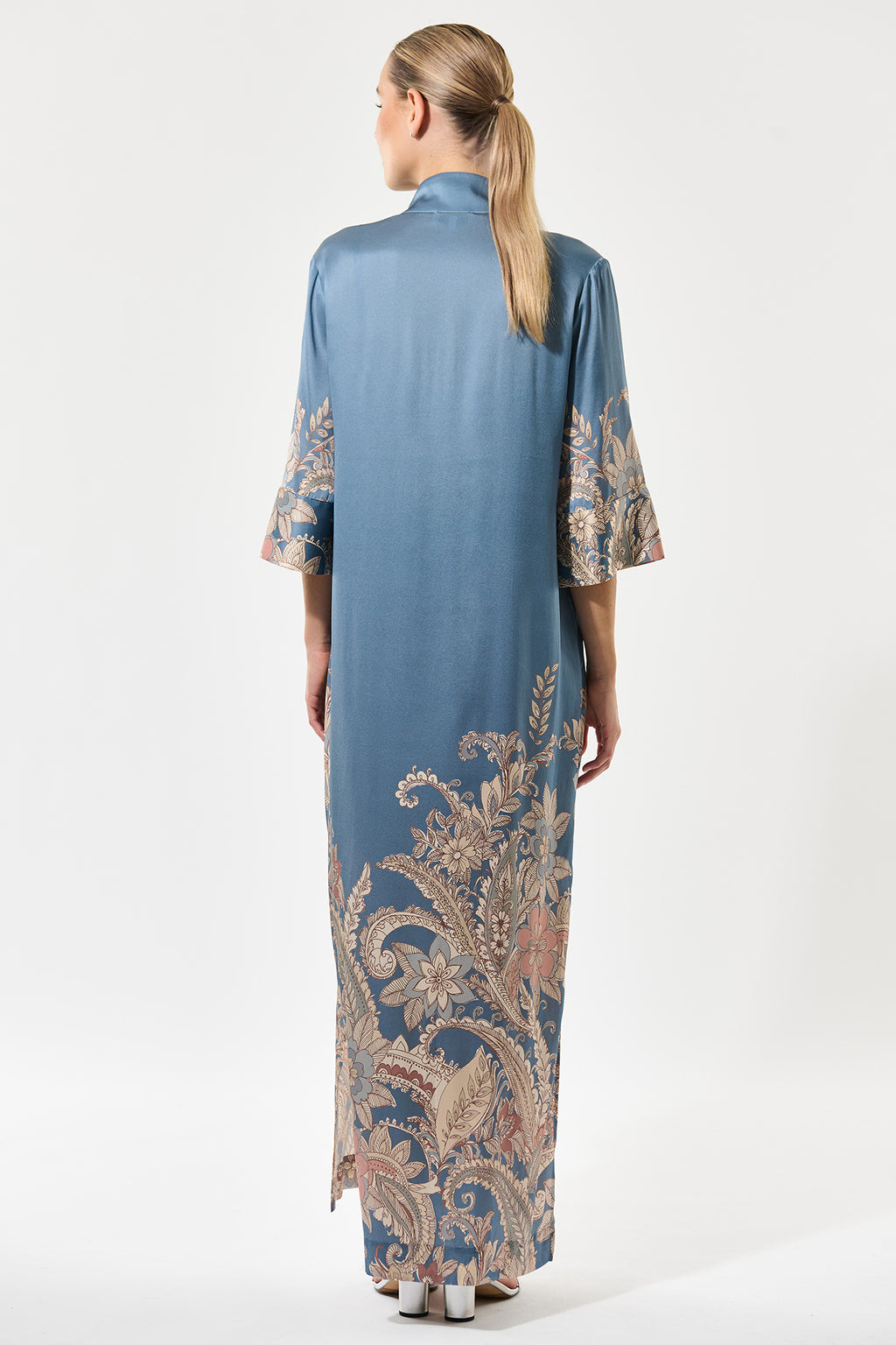 Woman wearing a long blue dress with intricate patterns on a white background