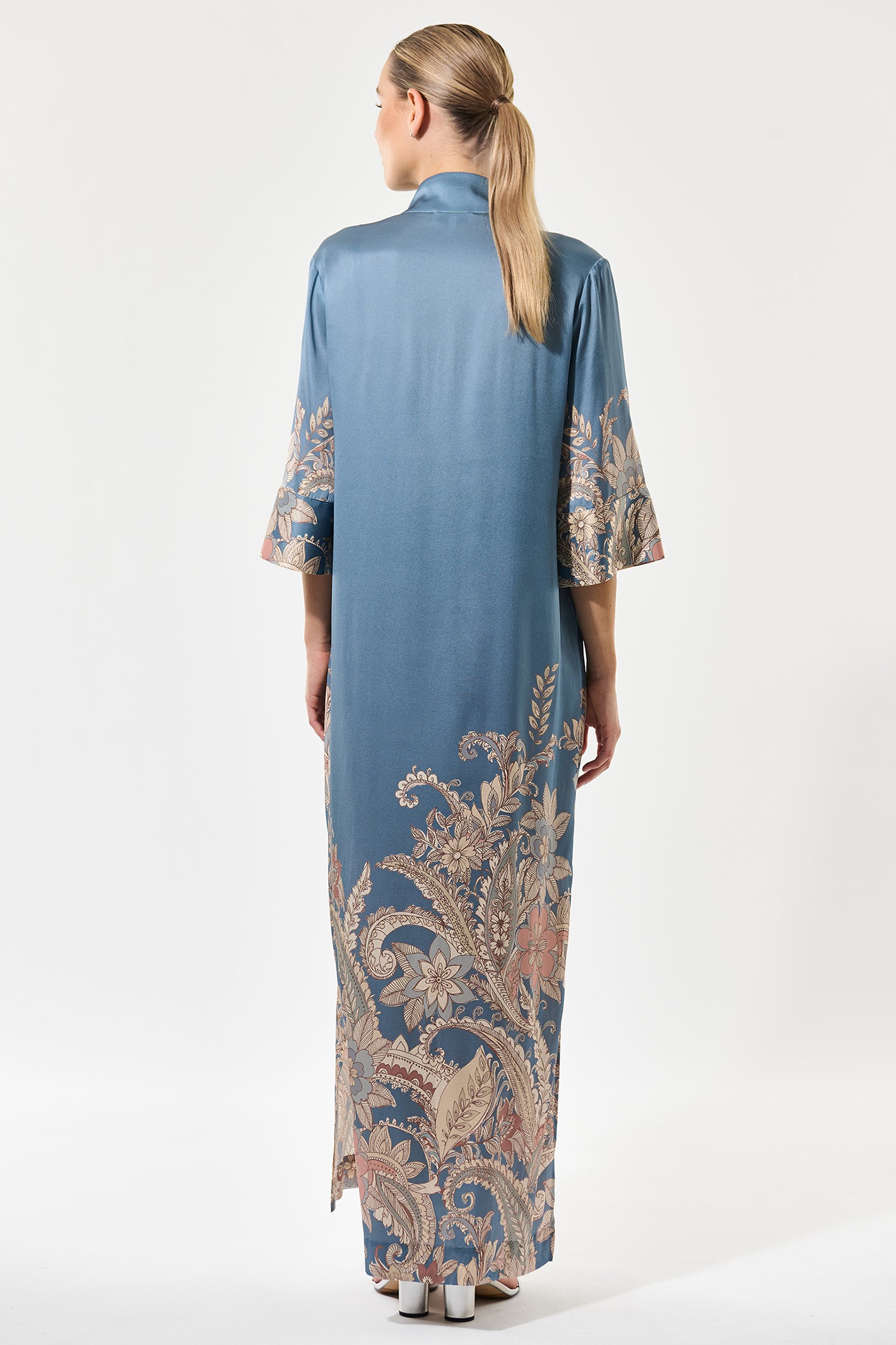 Woman wearing a long blue dress with intricate patterns on a white background