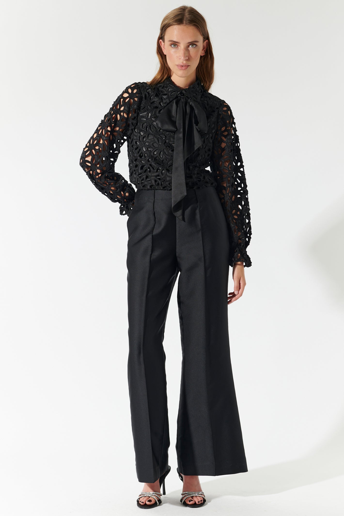 Woman wearing a black lace blouse with a bow and black pants on a white background