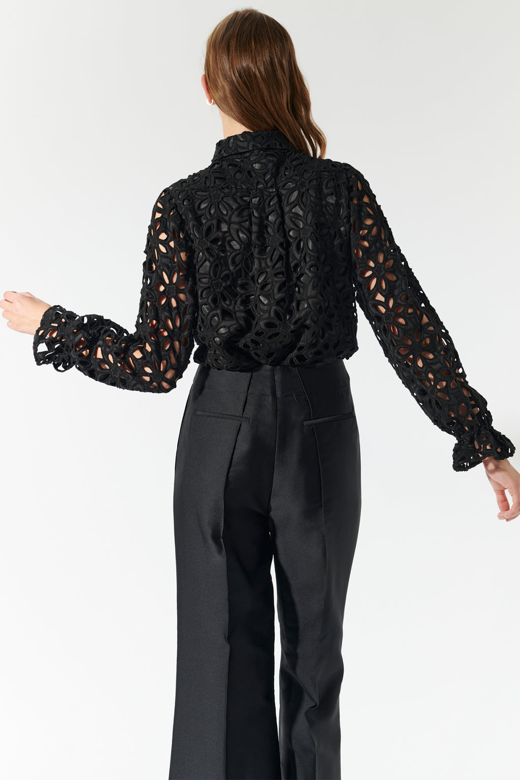 Person wearing a black lace top and black pants on a white background