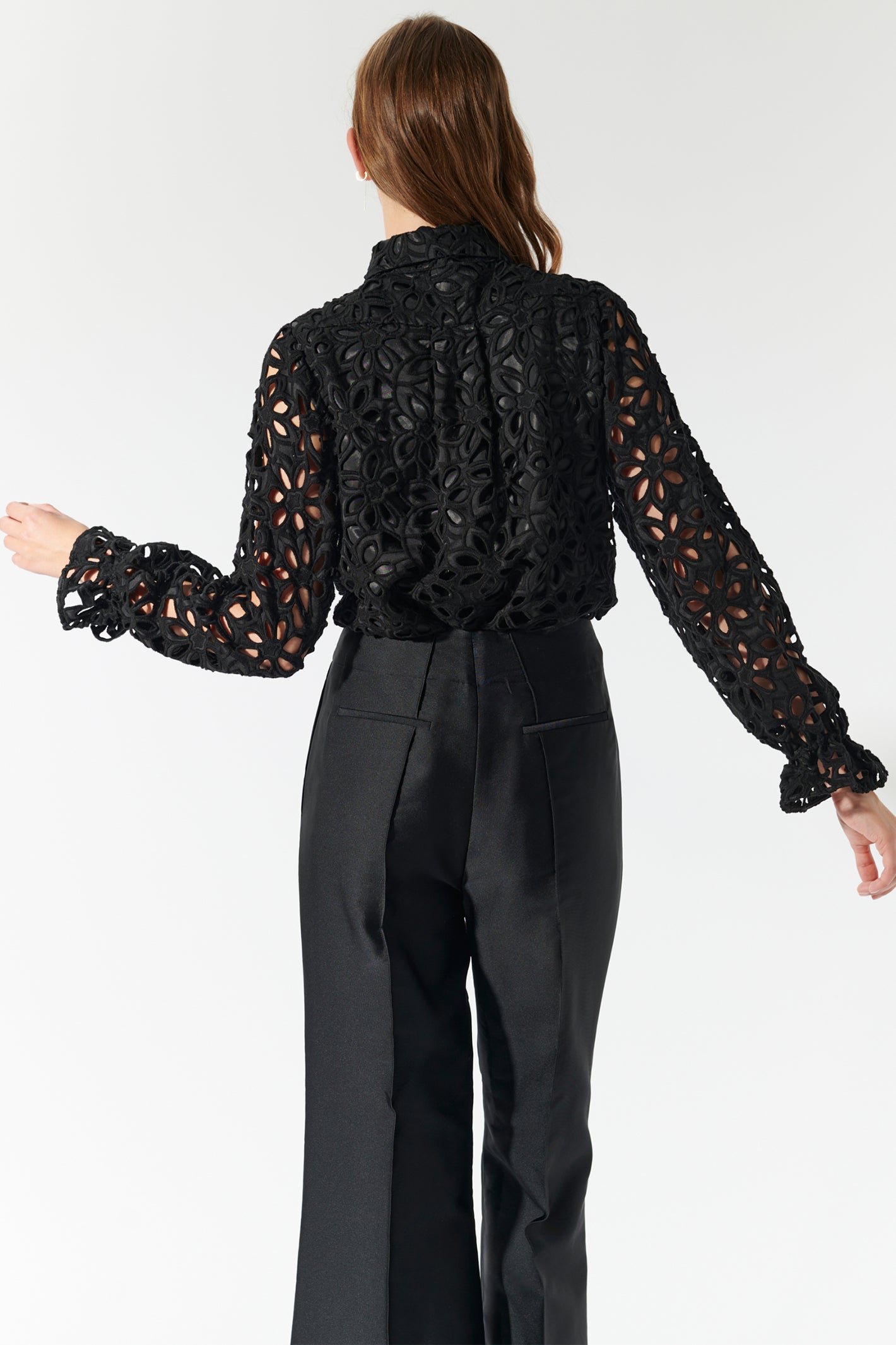 Person wearing a black lace top and black pants on a white background