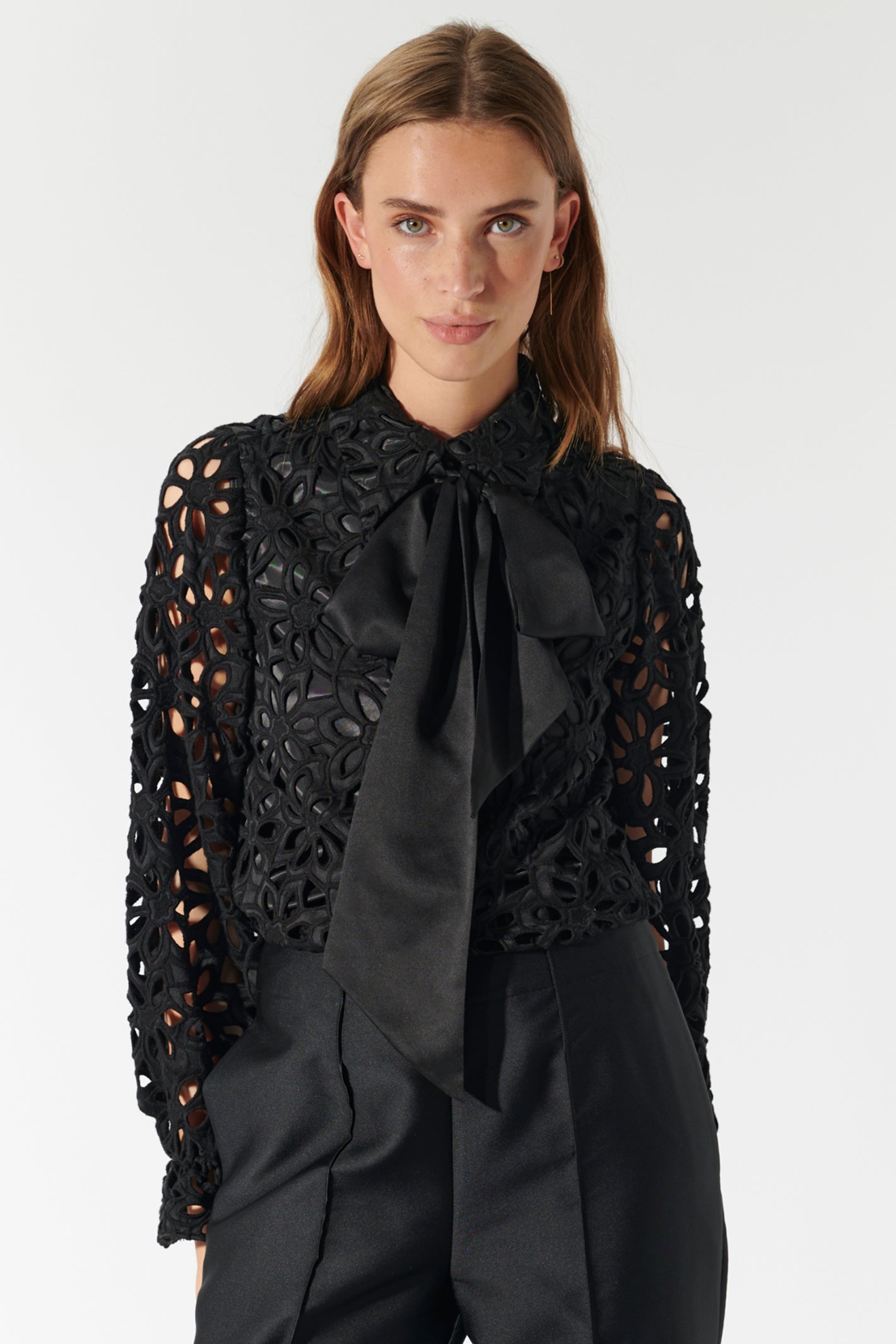 Woman wearing a black lace top with a large black bow tie on a white background
