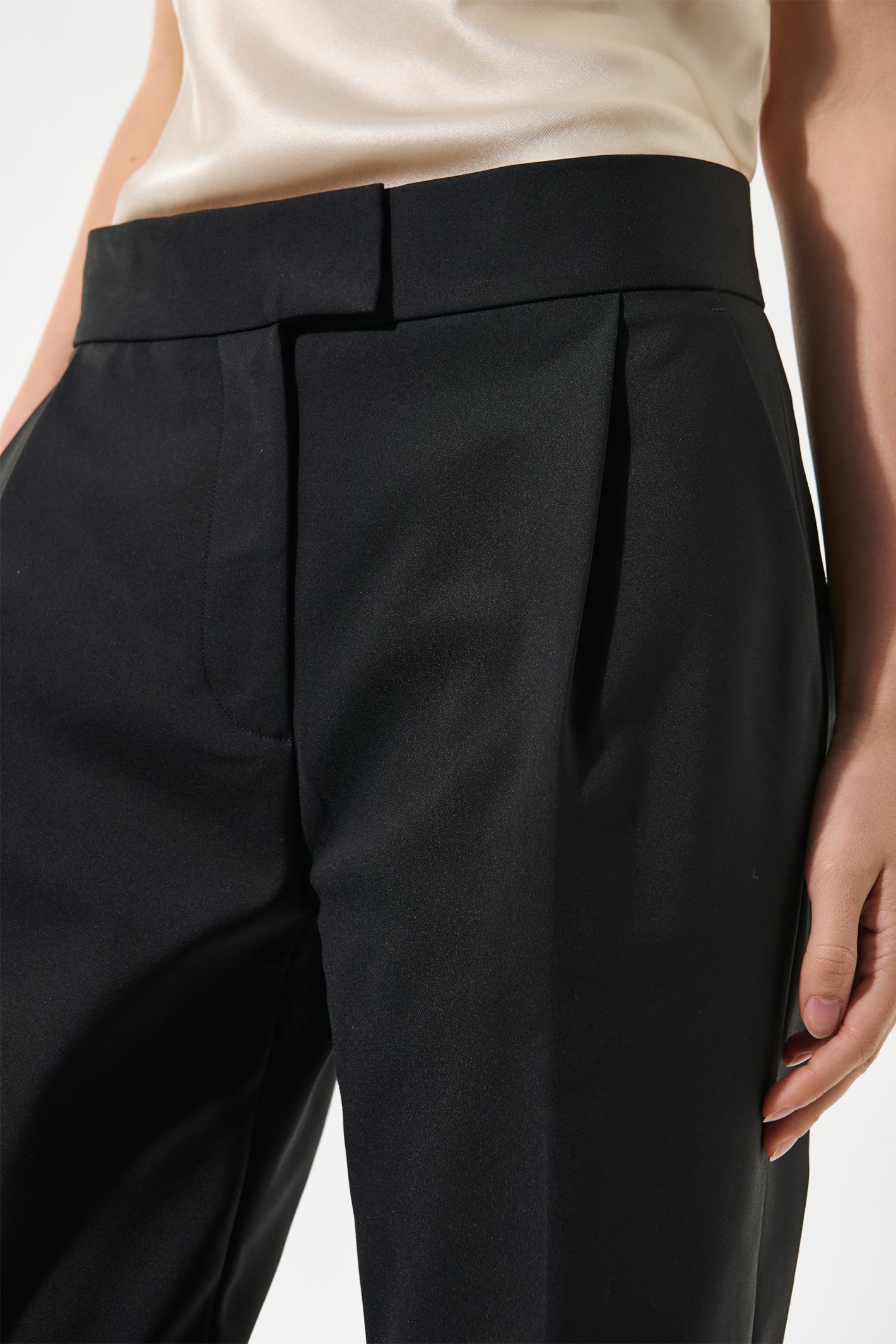 Black pleated pants worn by a person on a white background