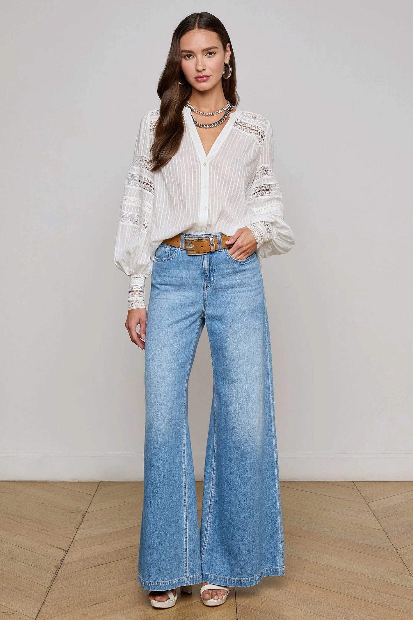 Woman wearing a white blouse and blue jeans against a plain background