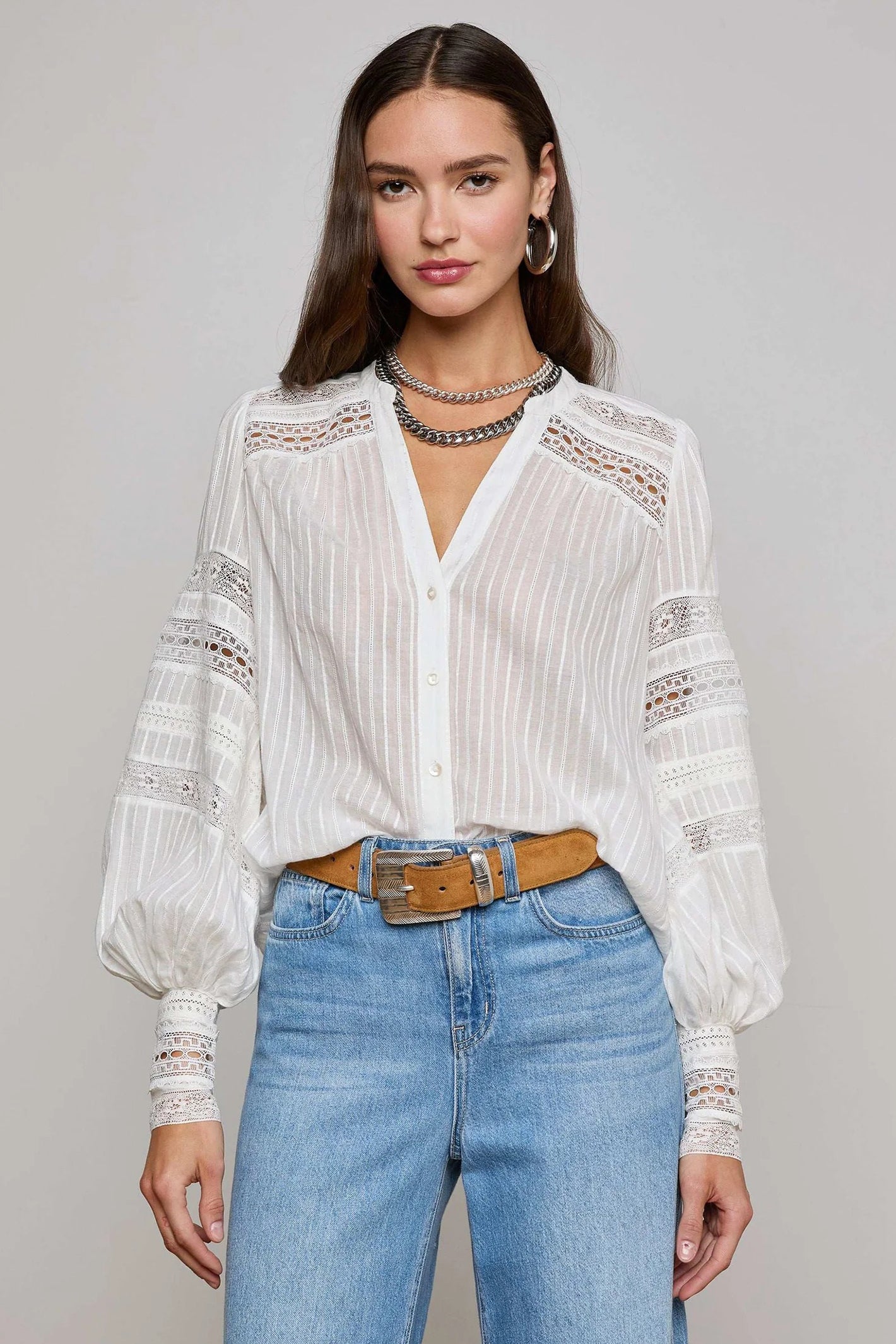 Woman wearing a white blouse with lace details and blue jeans on a plain background