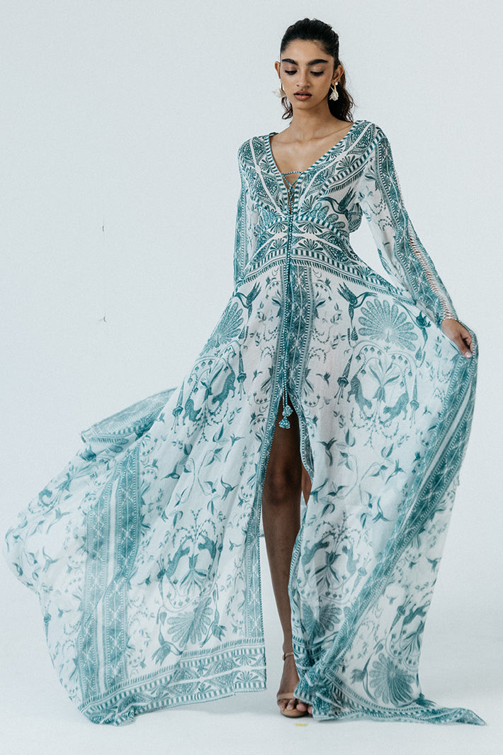 Woman wearing a long, light blue patterned dress against a white background