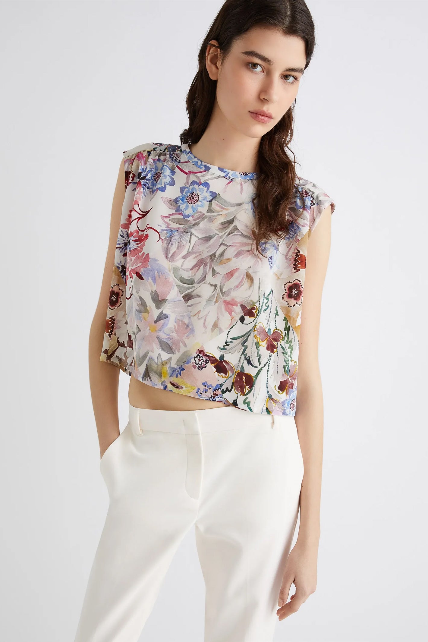 Woman wearing a sleeveless floral top and white pants on a white background