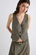 Woman wearing a green vest and pants with decorative brooches on a white background