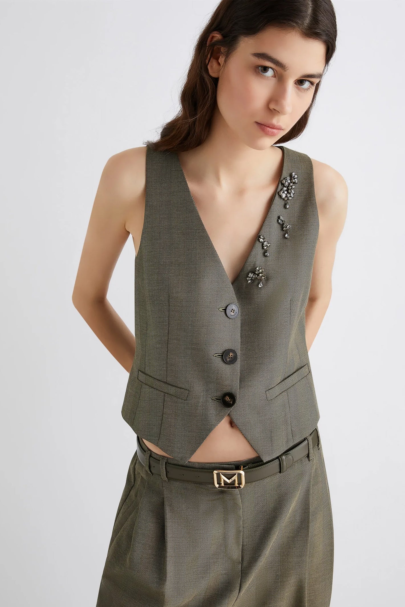 Woman wearing a green vest and pants with decorative brooches on a white background