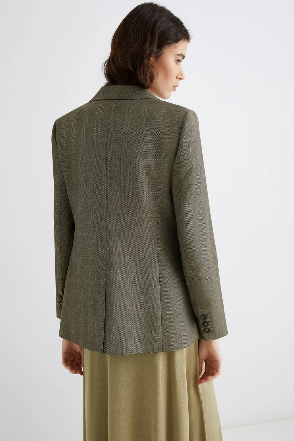 Woman wearing a green blazer and beige skirt against a white background