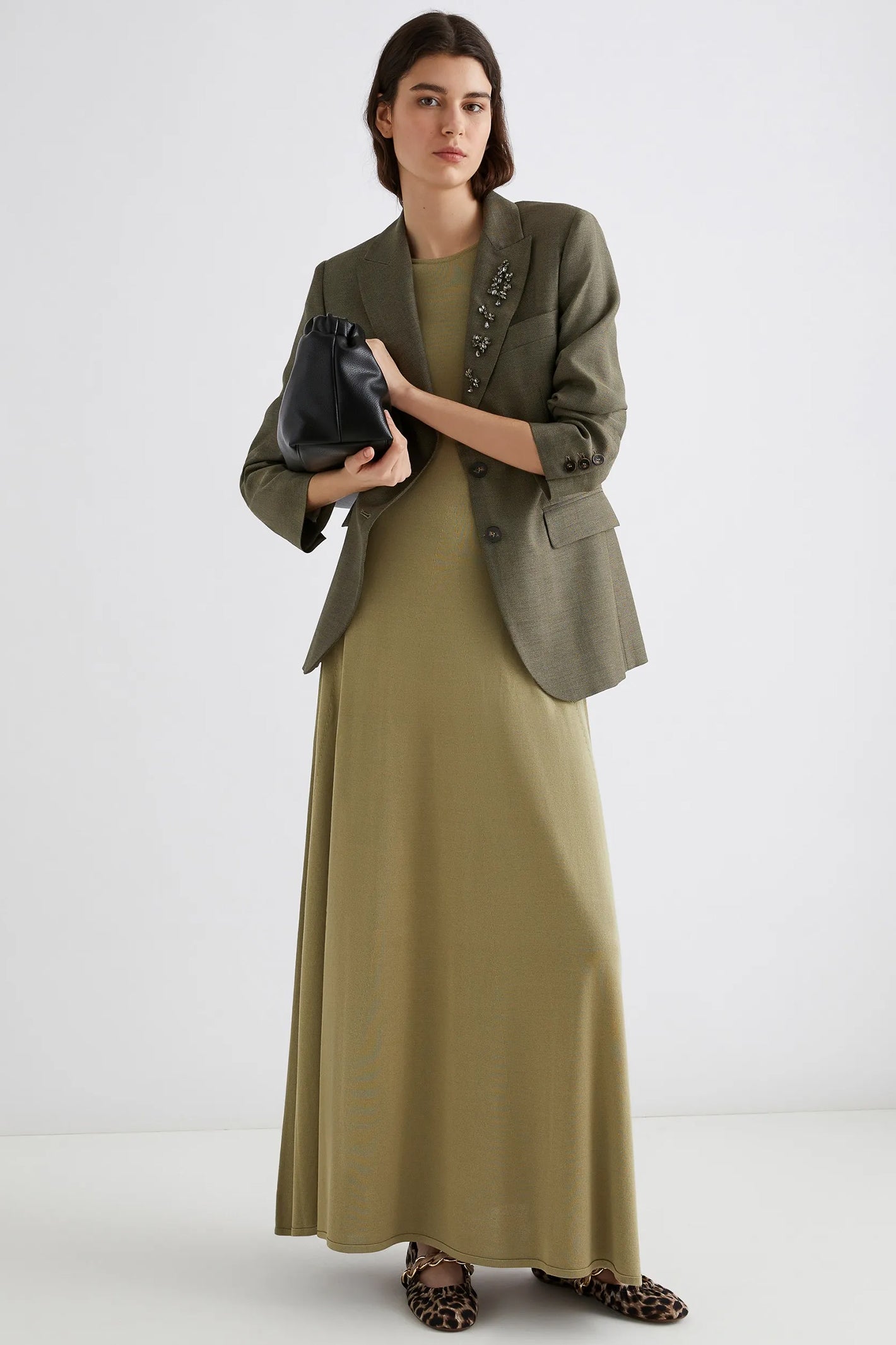 Woman wearing a green dress and jacket holding a clutch against a white background