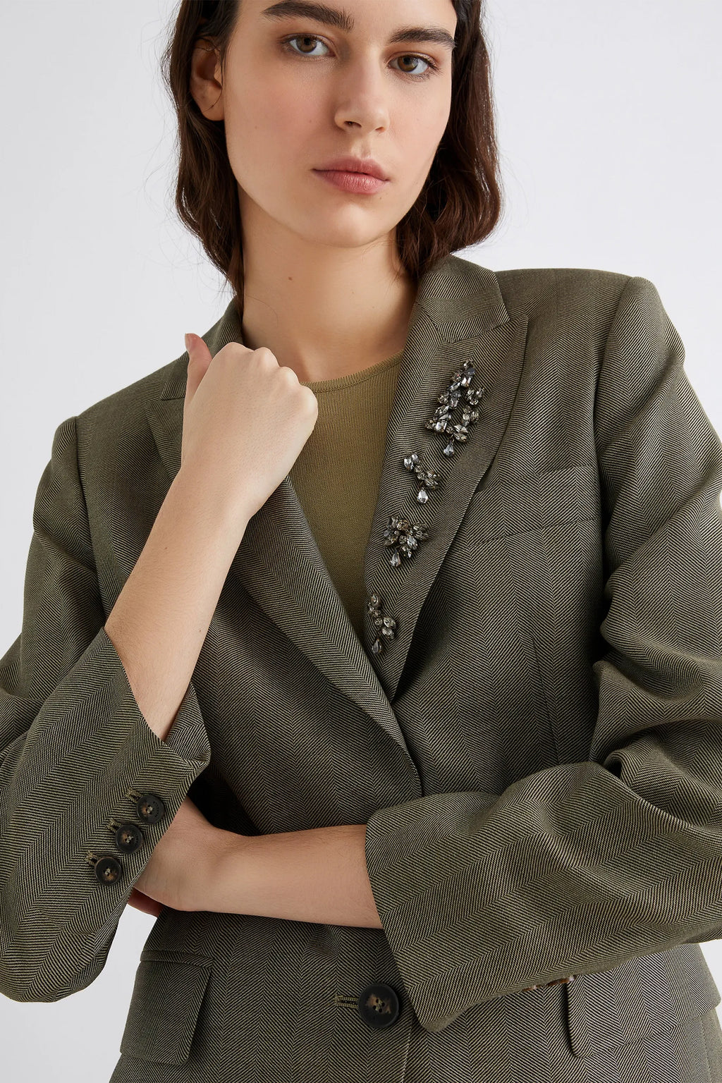 Woman wearing a green blazer with decorative buttons on a white background