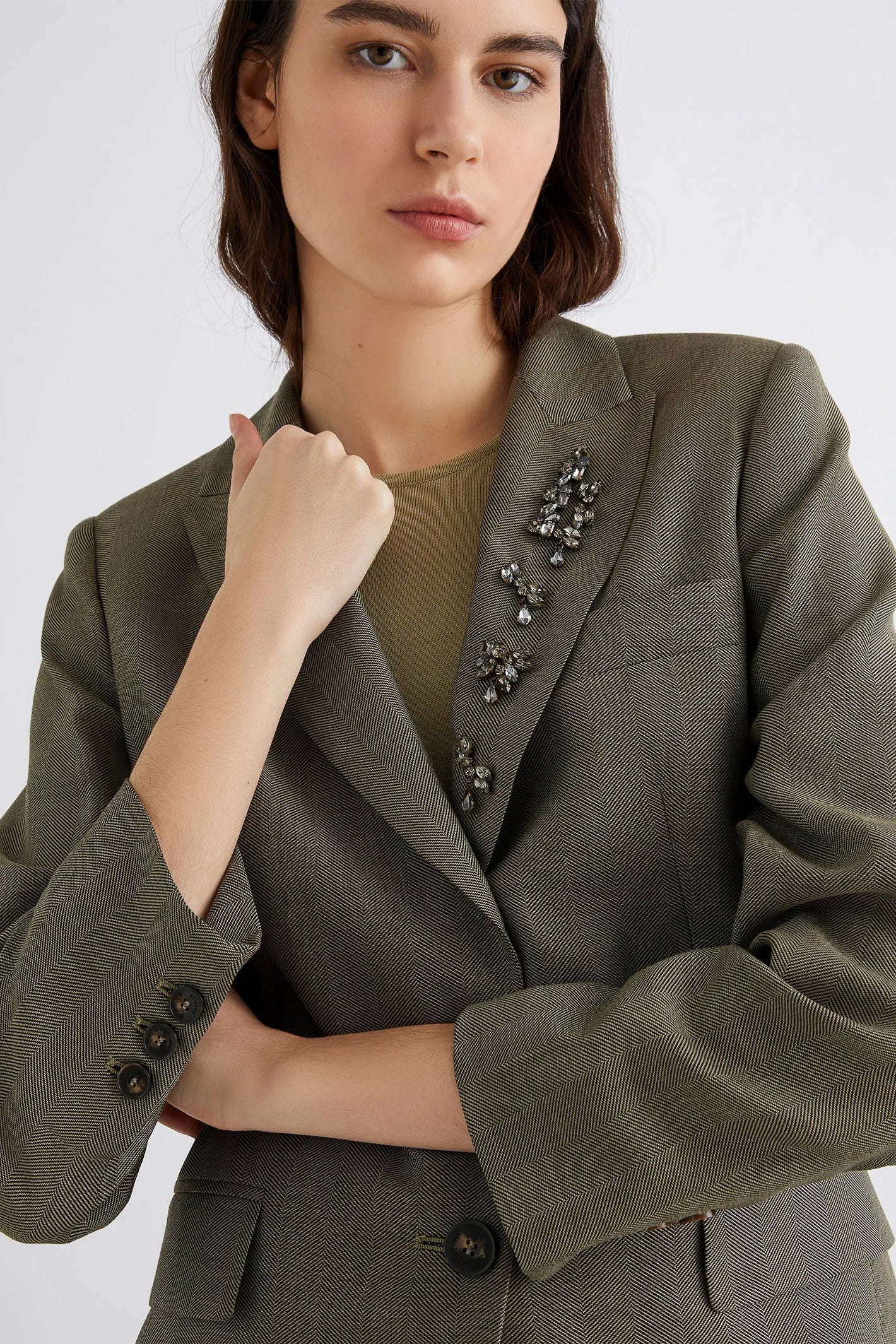 Woman wearing a green blazer with decorative buttons on a white background