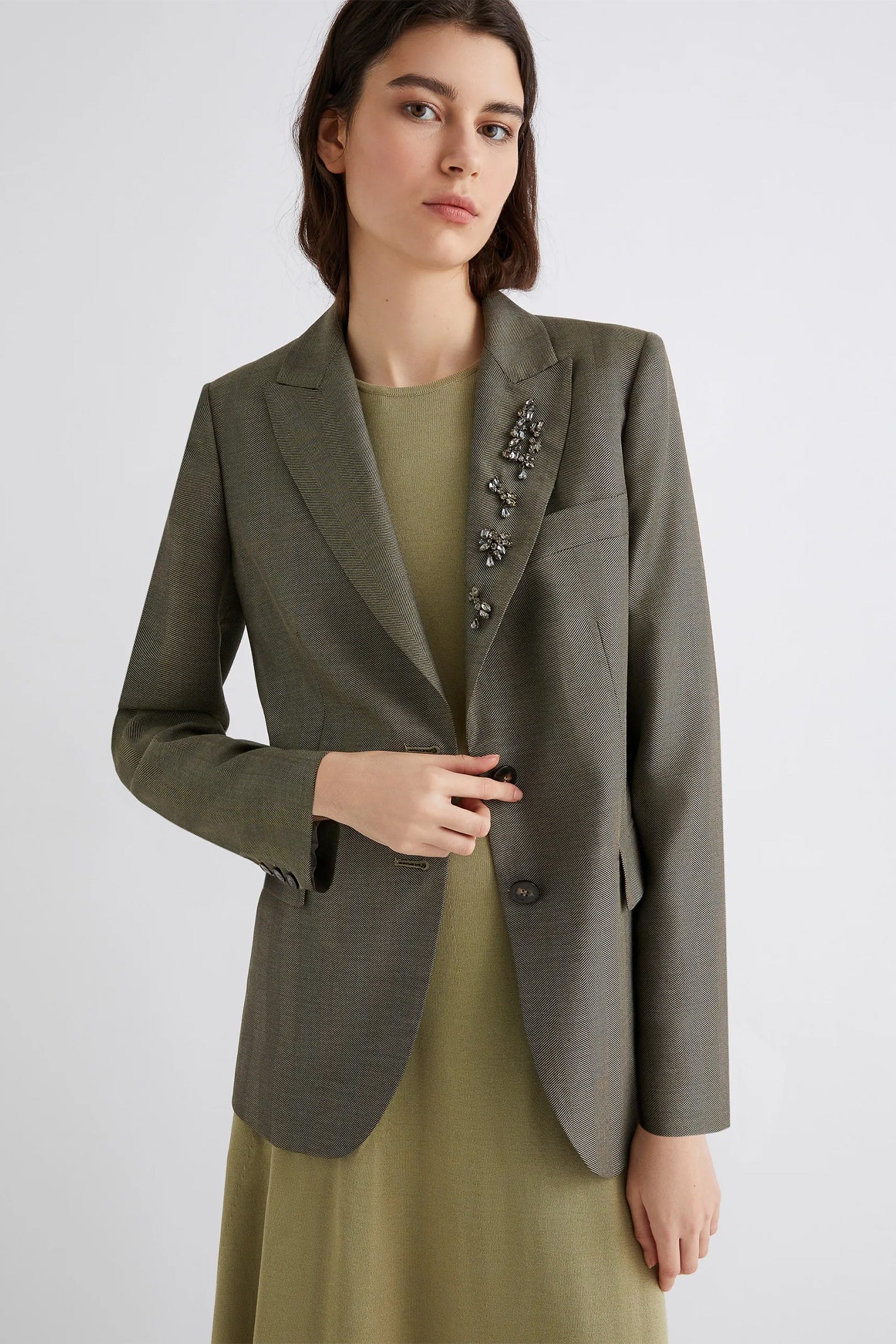 Woman wearing a green blazer with decorative buttons on a white background