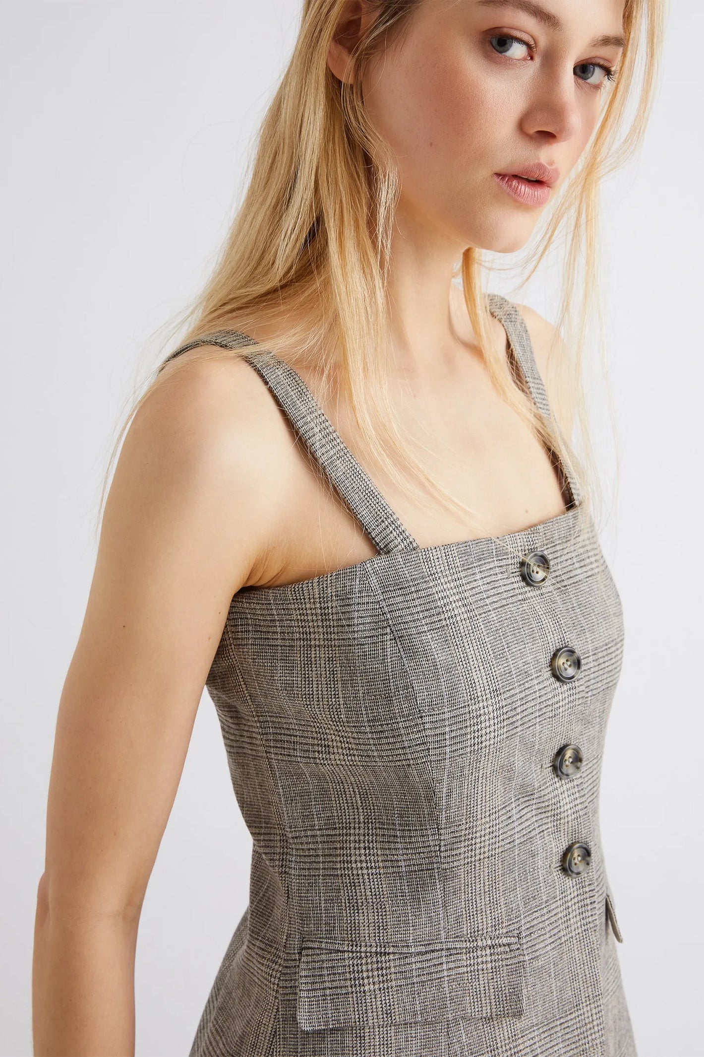 Woman wearing a gray checkered dress with button details on a white background