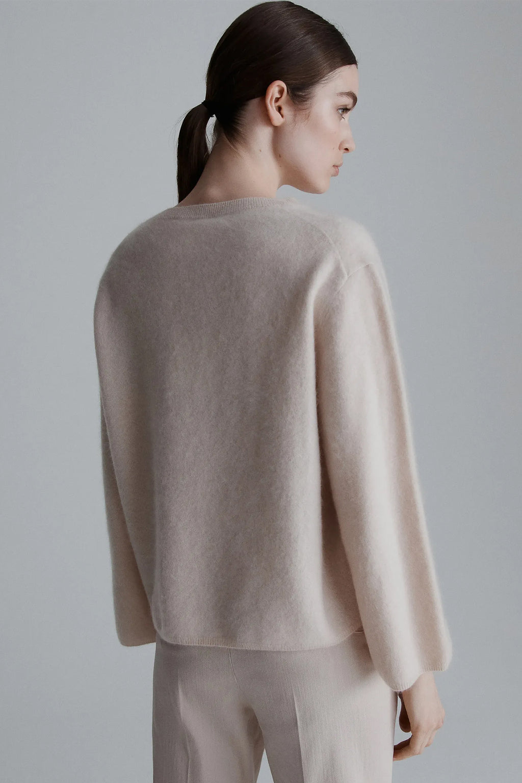 Woman wearing a beige sweater and pants against a gray background