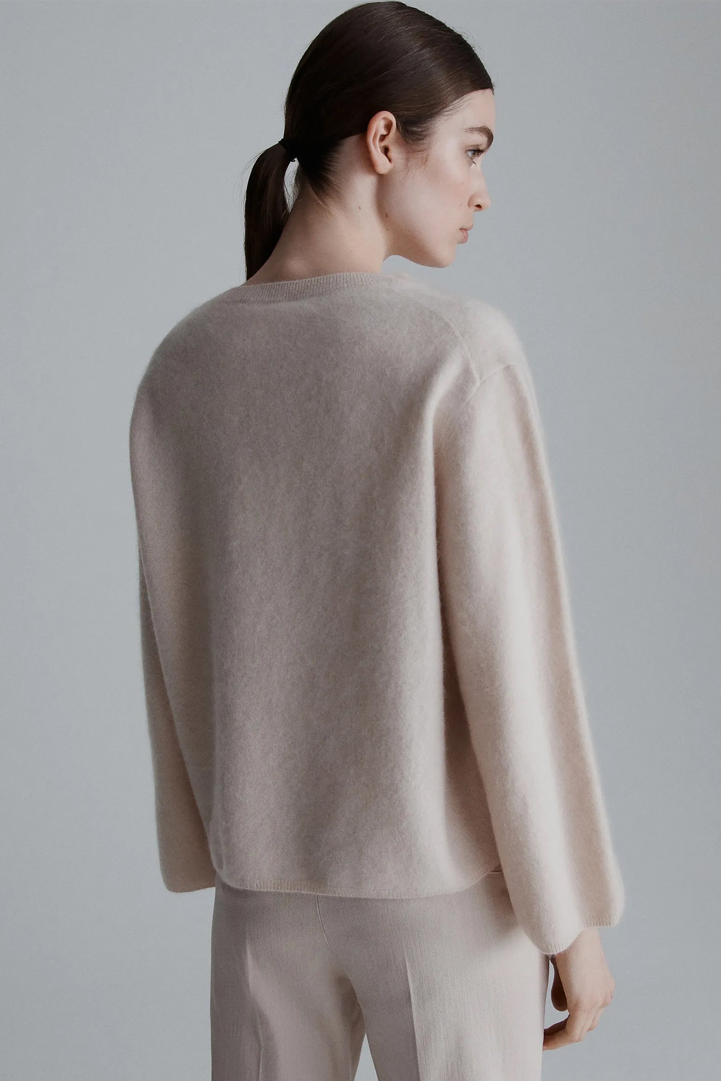 Woman wearing a beige sweater and pants against a gray background