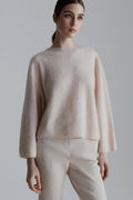 Woman wearing a beige sweater and pants against a plain background