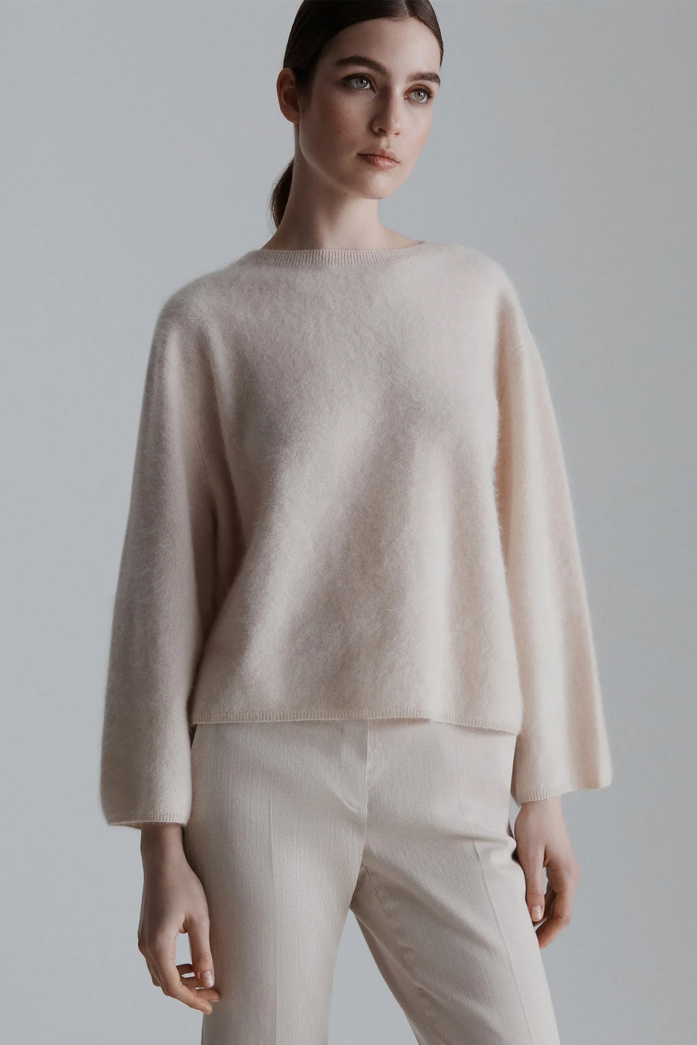 Woman wearing a beige sweater and pants against a plain background