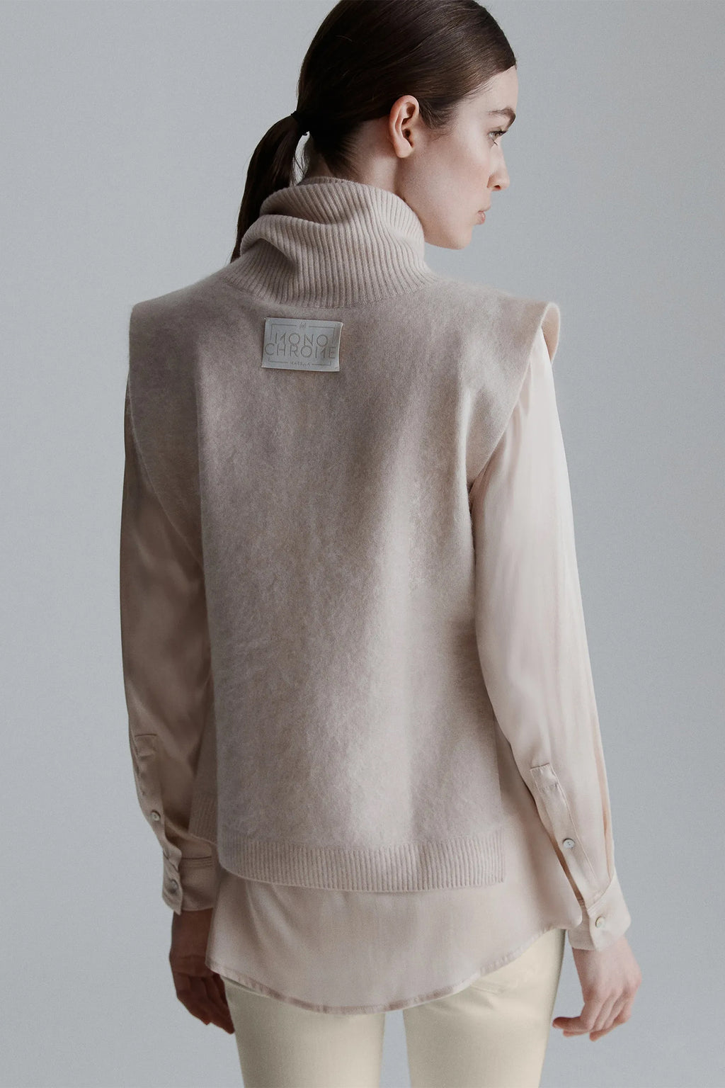 Woman wearing a beige sweater with a visible brand label on a plain background