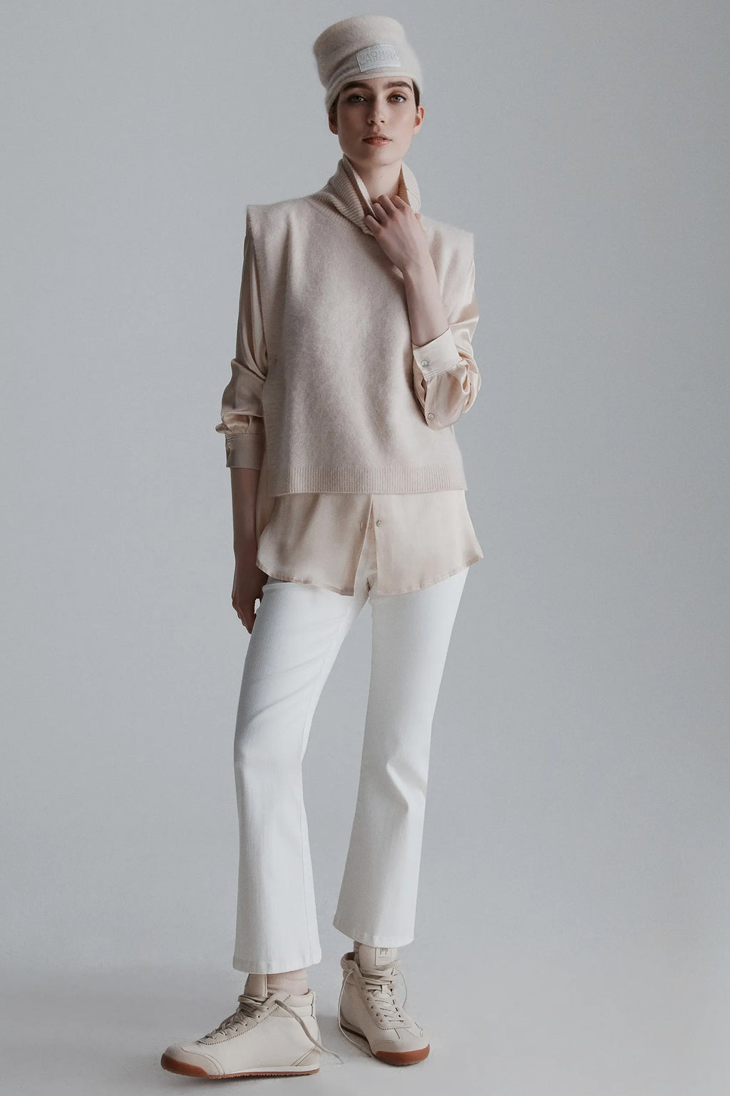 Person wearing a beige top, white pants, and a matching hat on a plain background