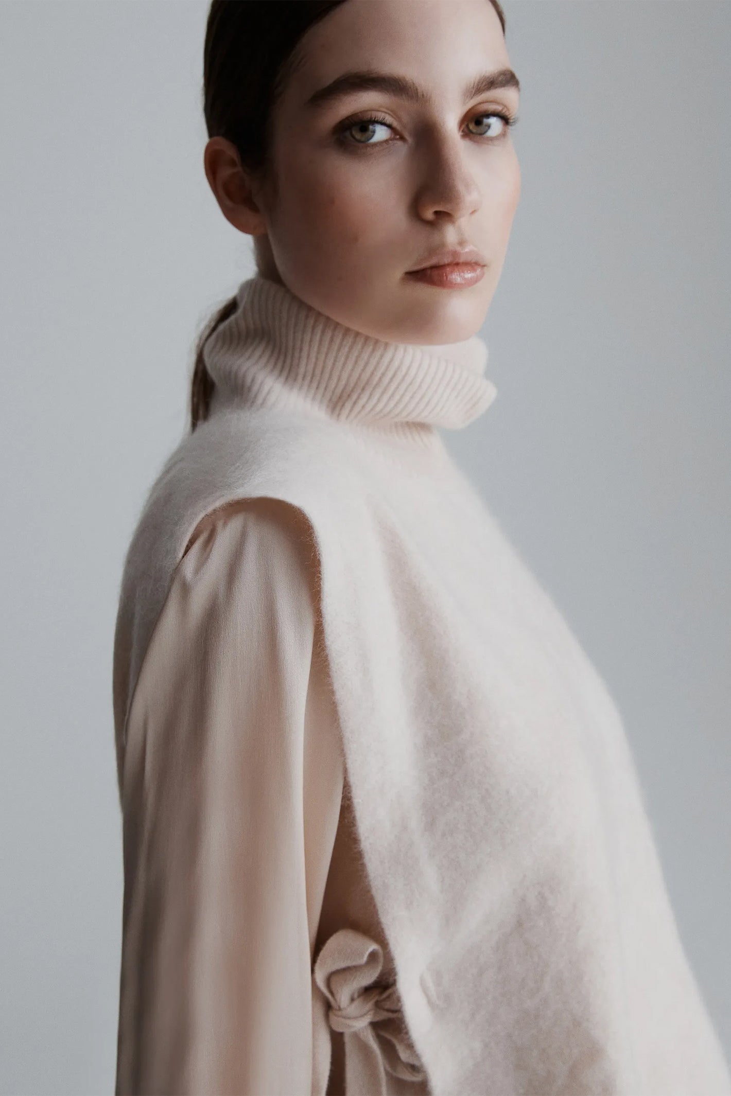 Woman wearing a beige turtleneck sweater against a plain background