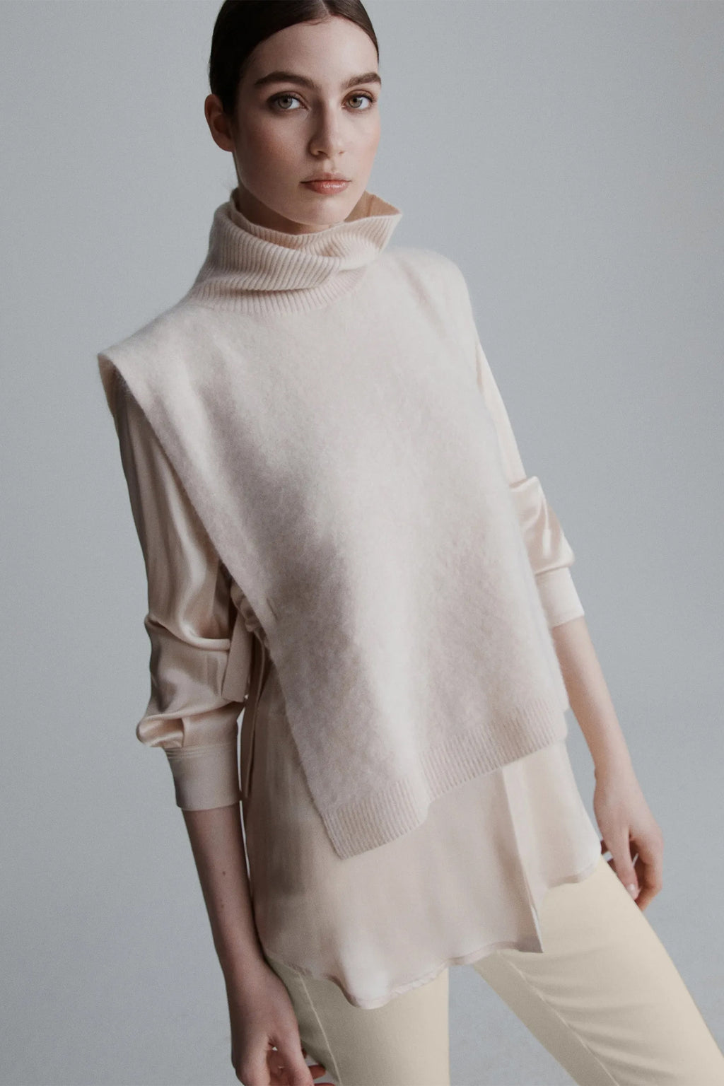 Woman wearing a beige turtleneck sweater with a cape over a plain background