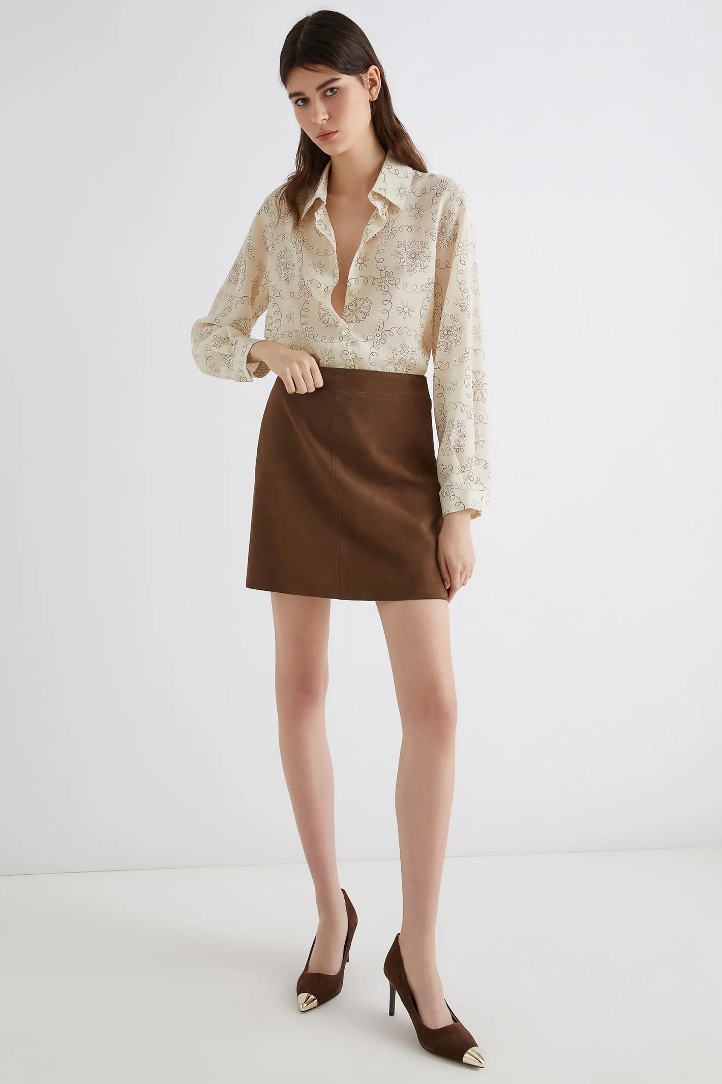Woman wearing a beige blouse and brown skirt on a white background