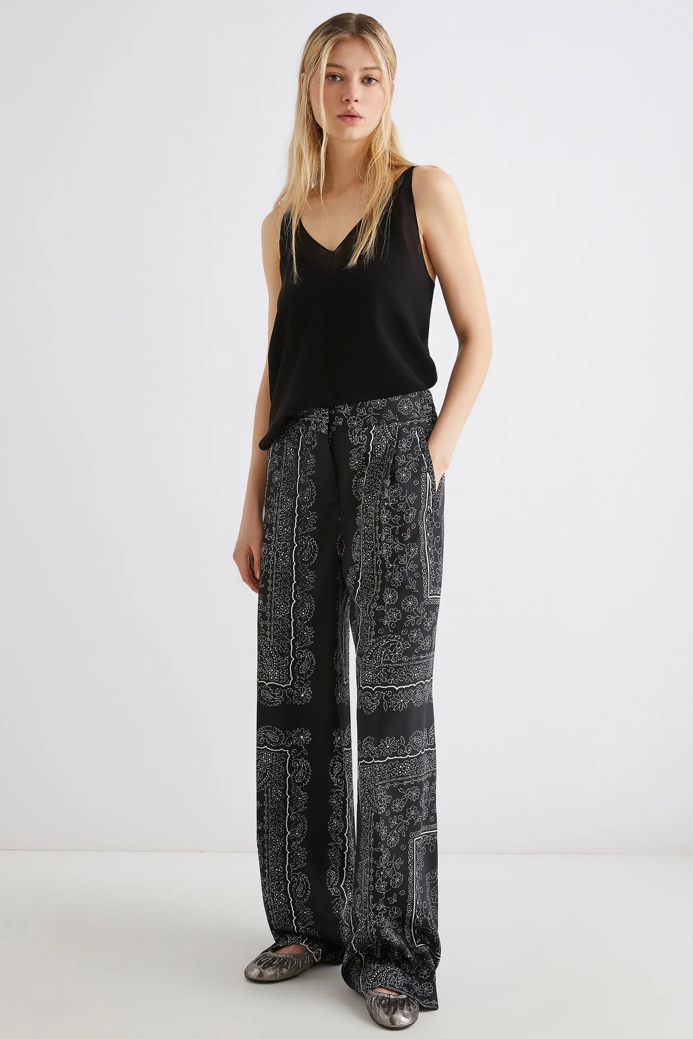Woman wearing a black sleeveless top and patterned pants on a white background