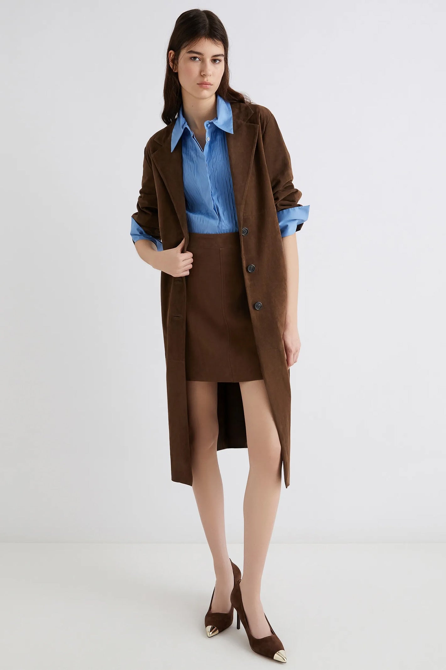 Woman wearing a brown coat, blue shirt, and skirt on a white background