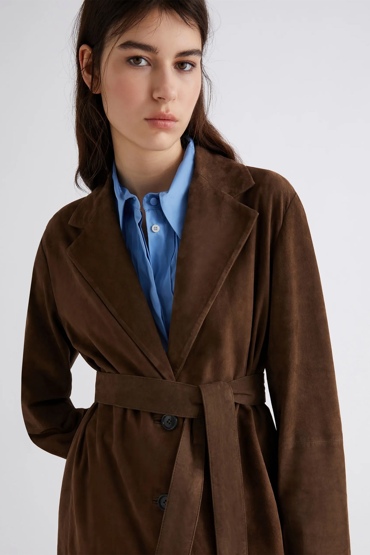 Woman wearing a brown coat over a blue shirt on a white background